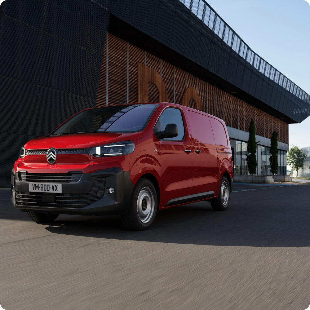 Driekwart vooraanzicht van een rode Citroën Jumpy rijdend in een stedelijke omgeving, met modern design, rijcomfort, connectiviteit en een zelfverzekerde professionele uitstraling.