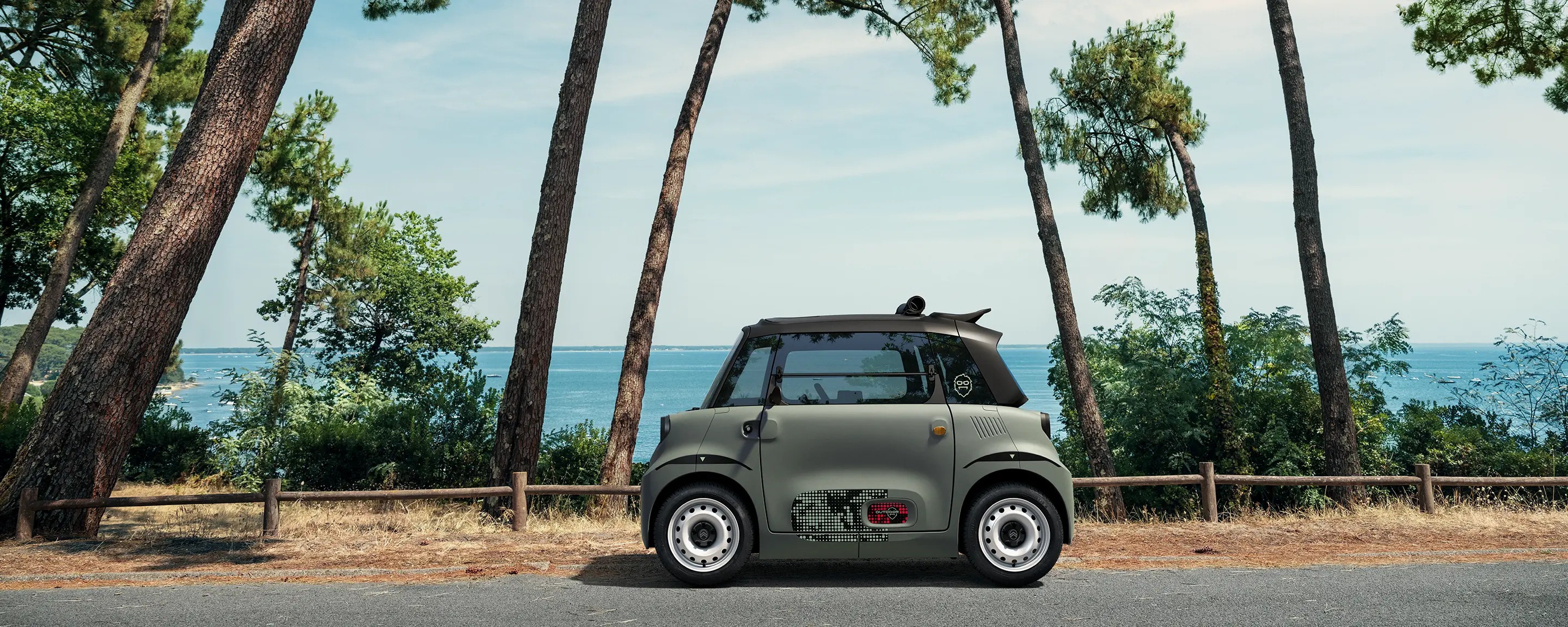 Zijaanzicht van de Citroën ami Outdoor met open dak toont de ultracompacte elektrische stadsauto aan zee