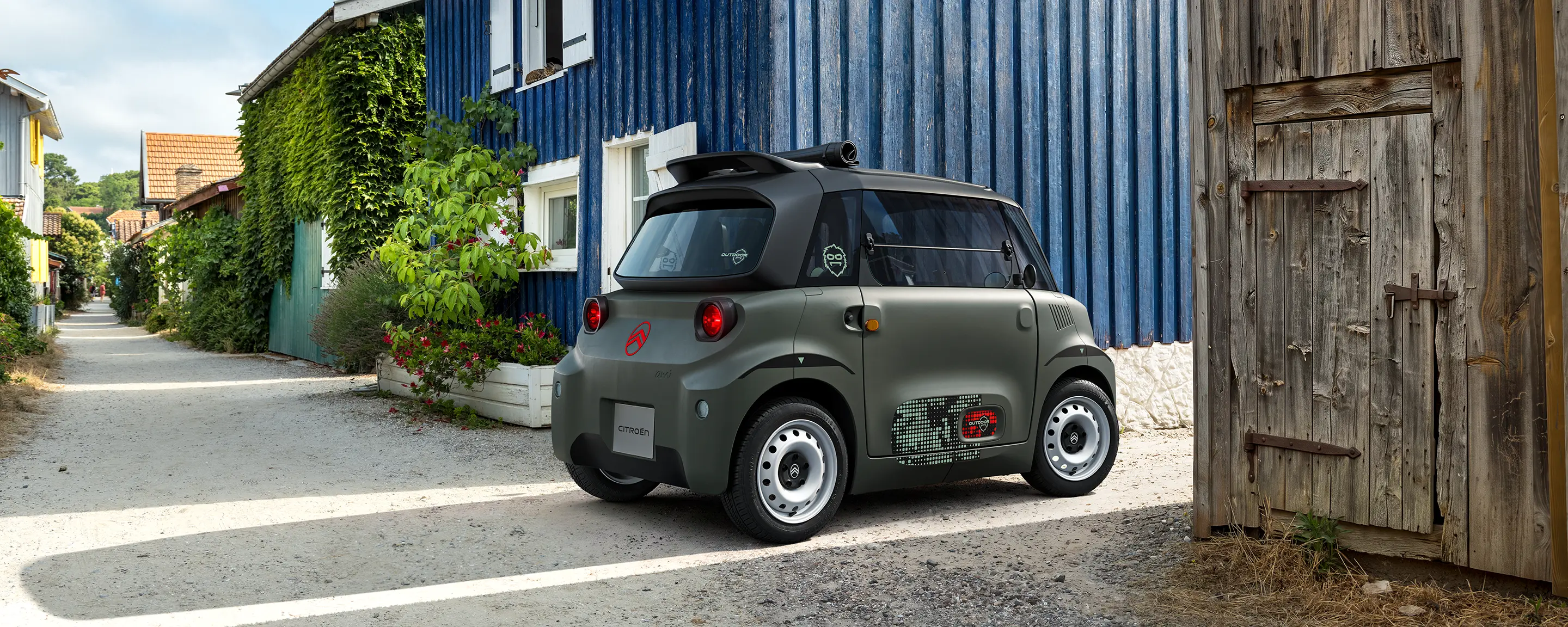 Driekwartvooraanzicht van de Citroën ami Outdoor met led-koplampen toont een compacte elektrische stadsauto in een kustdorpje