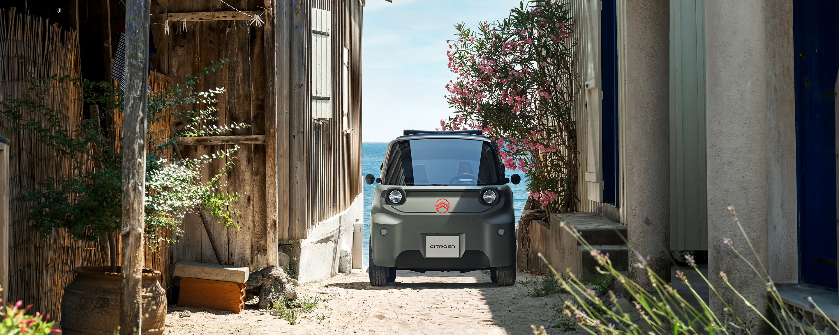 Vooraanzicht van de Citroën ami Outdoor met led-koplampen: een compacte elektrische stadsauto die door een smal kustweggetje rijdt