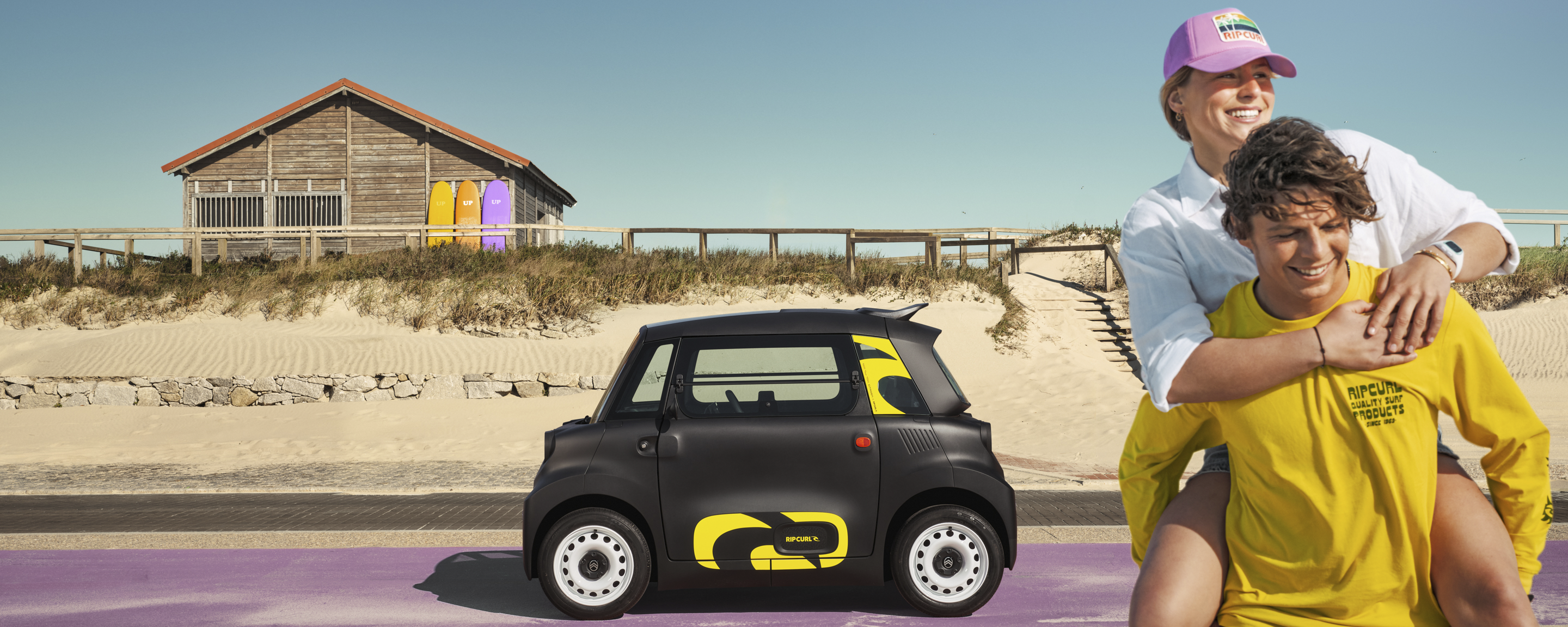 Zijaanzicht in lifestyle‑setting van de Citroën Ami x Rip Curl, elektrische auto zonder autorijbewijs, met vrijheid aan zee.