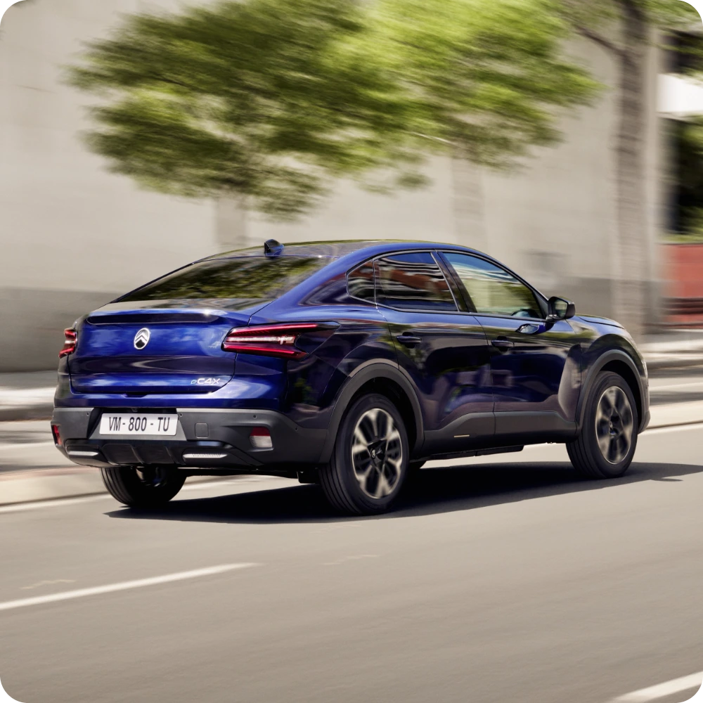 Driekwart achteraanzicht van de Citroën ë‑C4 X rijdend in de stad, ter illustratie van het grotere elektrische rijbereik.