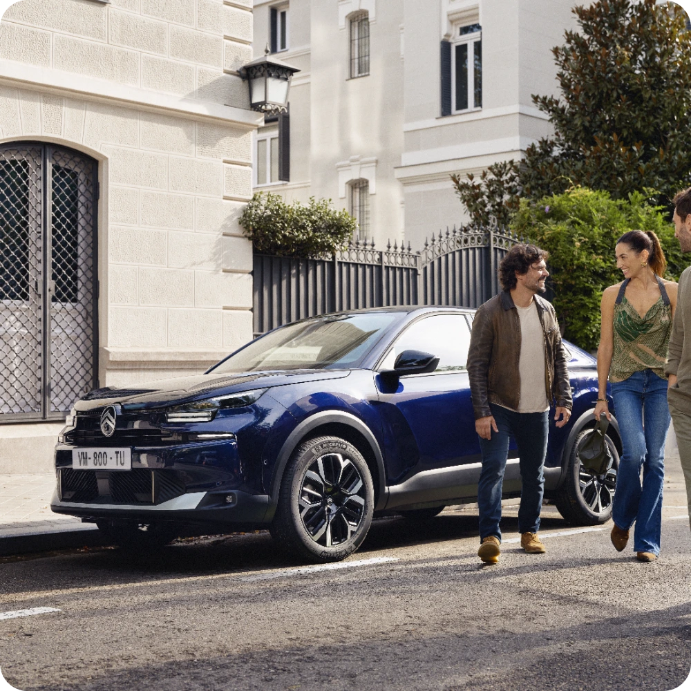 De Citroën C4 X Hybrid geparkeerd voor een gebouw met passagiers, waarbij slimme en efficiënte hybridetechnologie zichtbaar is.