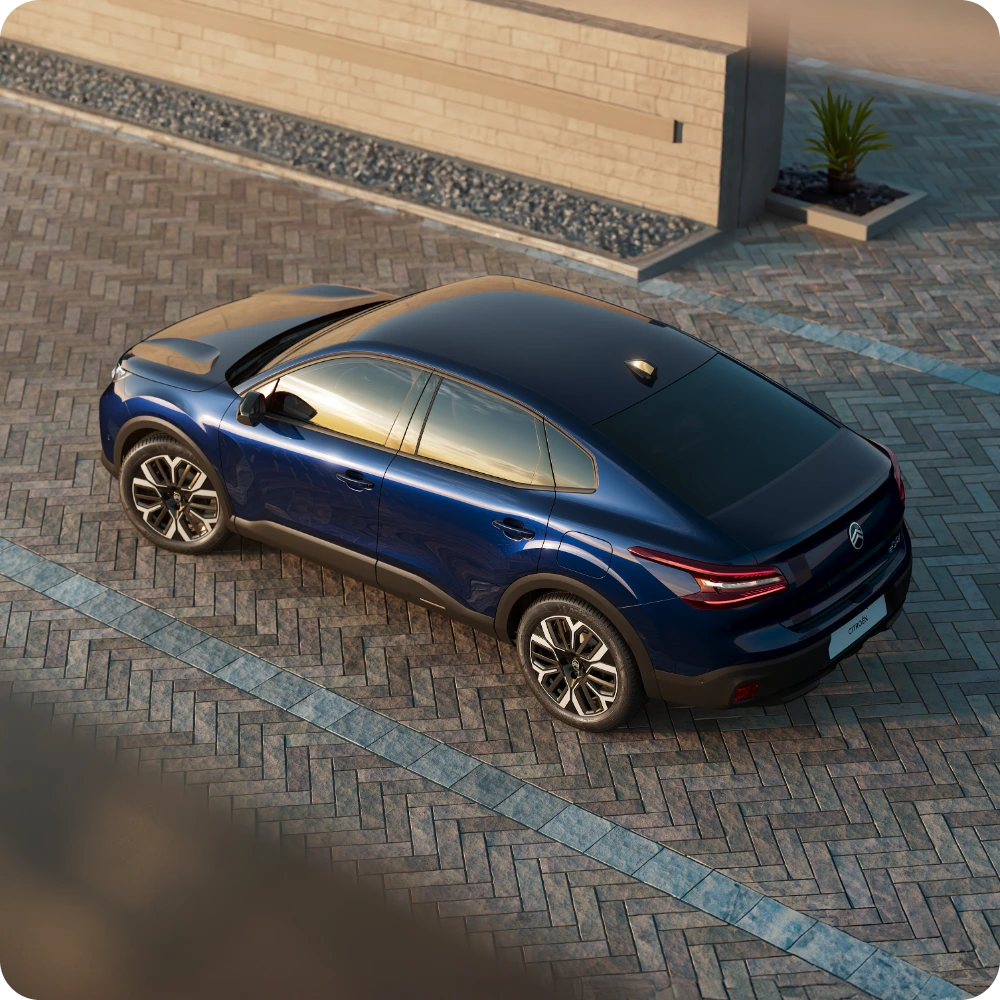 Bovenaanzicht van de Citroën C4 X geparkeerd bij een moderne wand, met een onderscheidend en strak design.
