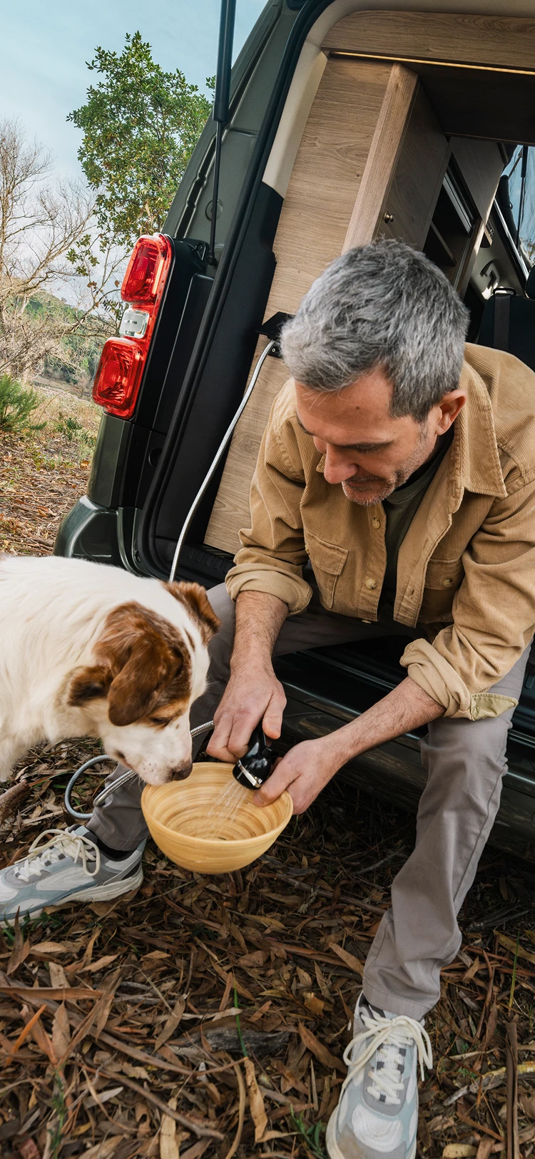 Man geeft een hond eten vanuit de achterdeur van een Citroën camper van midden in de natuur