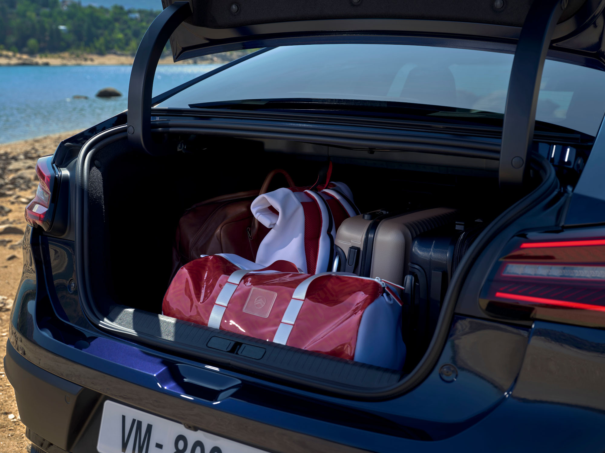 Open bagageruimte van de Citroën C4 X gevuld met reistassen naast een locatie aan een meer.