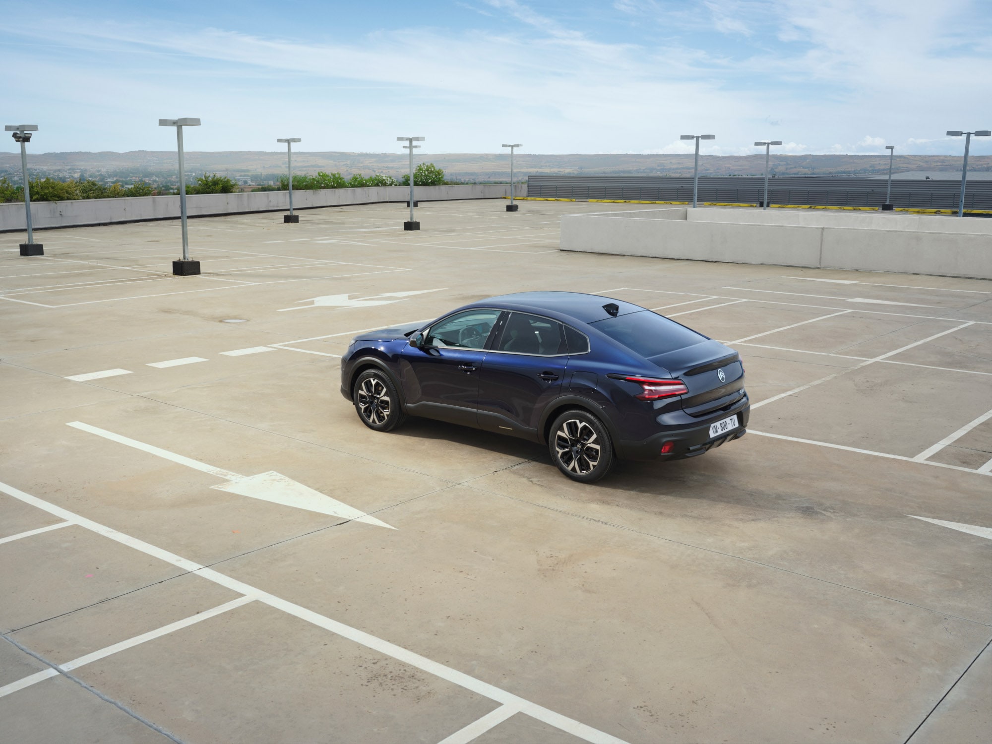 Driekwart achteraanzicht van de Citroën C4 X op een open dak parkeerterrein met elegante fastback‑lijnen voor betaalbare mobiliteit.
